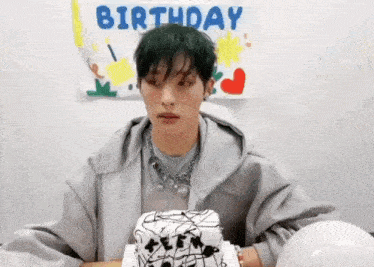 a young man is sitting at a table with a birthday cake in front of him .