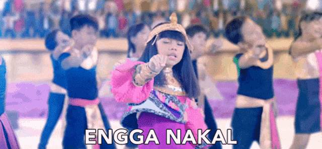 a girl in a pink dress is dancing in front of a crowd with the words " engo nakal " written below her