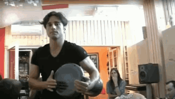 a man in a black shirt is holding a drum in a living room .