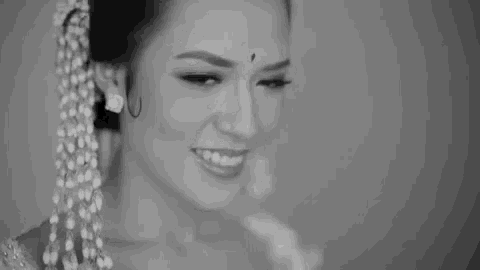 a black and white photo of a woman smiling and wearing a flower in her hair .