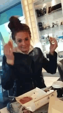 a woman in a black jacket is sitting at a table with a box of food in front of her