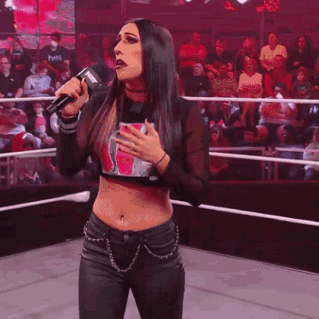 a woman is singing into a microphone in a wrestling ring with a crowd watching
