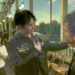 a man in a black jacket with the word vincent on it is talking to another man
