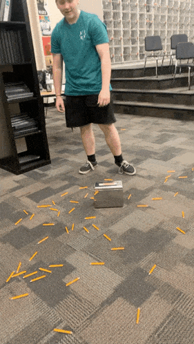 a man in a blue shirt is standing next to a box of pencils