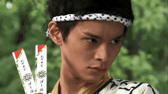a young man wearing a headband and holding two chopsticks with chinese writing on them
