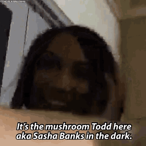 a man with a beard is standing in a dark room and talking about mushrooms .