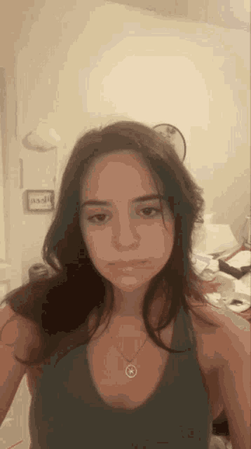 a woman wearing a necklace and a tank top looks at the camera