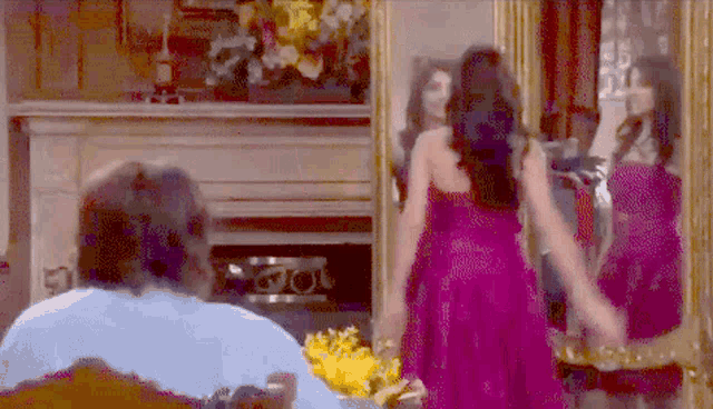a woman in a purple dress is standing in front of a fireplace