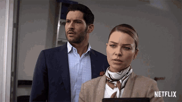 a man in a suit and a woman in a scarf are standing next to each other with a netflix logo in the background