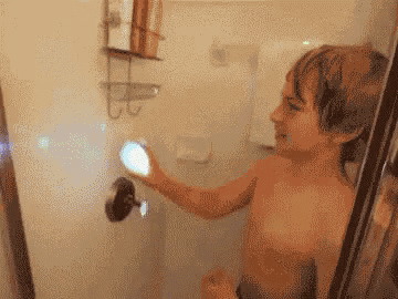 a shirtless young boy is taking a shower in a bathroom .