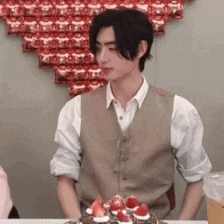 a man in a vest is standing in front of a birthday cake .