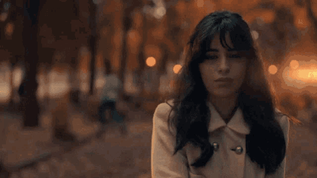 a woman in a white coat stands in a park