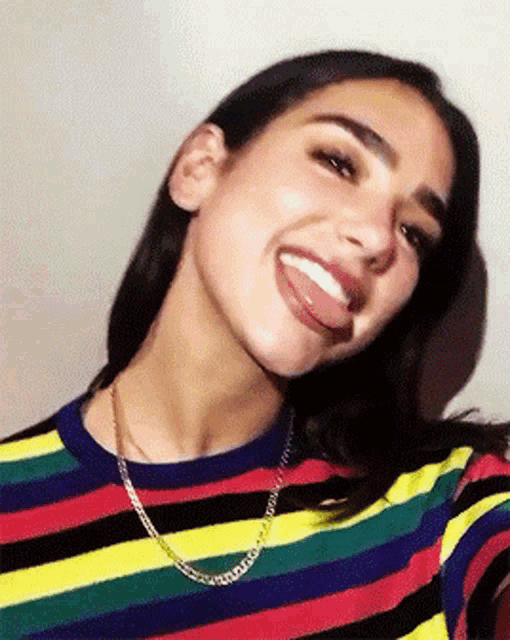 a woman wearing a striped shirt and a chain sticks out her tongue