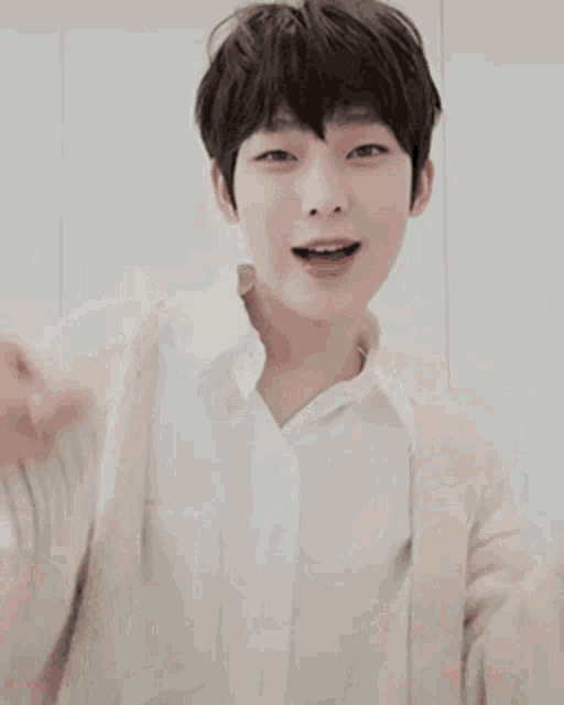 a young boy wearing a white shirt and a beige cardigan is smiling and pointing .