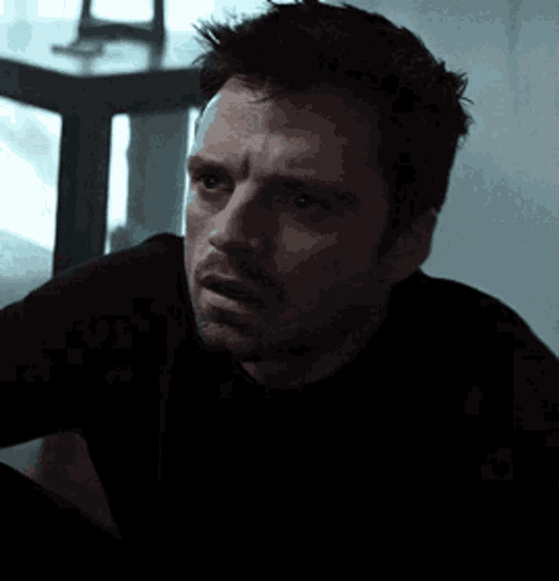 a man with a beard is wearing a black sweater and looking at the camera .