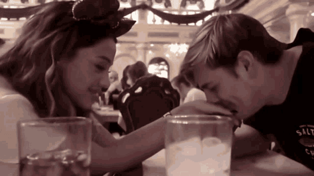 a man kisses a woman 's hand while sitting at a table with a glass of water in front of them