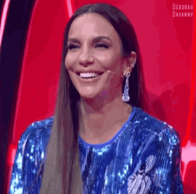 the woman is wearing a blue sequined dress and earrings and is smiling .