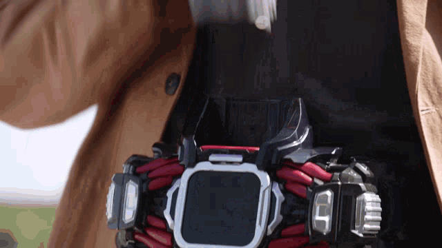 a person wearing a brown coat and a black shirt has a belt on their waist that looks like a watch
