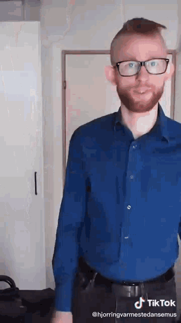 a man with glasses and a beard is wearing a blue shirt .