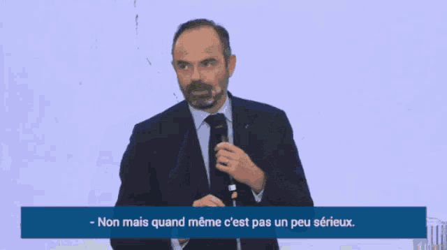 a man in a suit holds a microphone and says non mais quand meme c est pas un peu sérieux