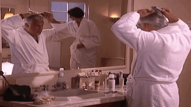 a man in a bathrobe looks at his reflection in a mirror