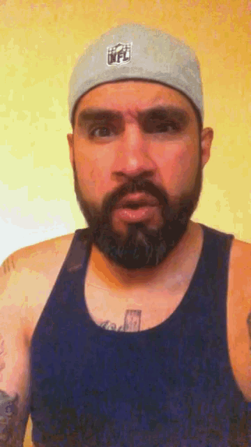 a man with a beard wearing a nfl hat and a blue tank top