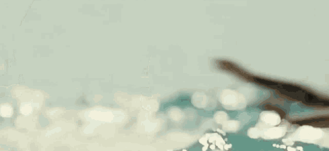 a man is swimming in the ocean without a shirt on and splashing water on his face .