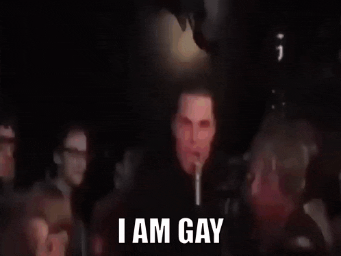 a man is standing in front of a microphone in a dark room and says `` i am gay '' .