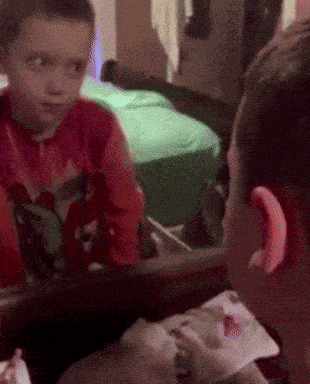 a boy in a red shirt looks at himself in the mirror