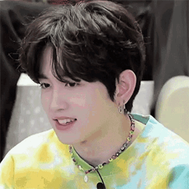 a young man wearing a tie dye shirt and a necklace with beads is smiling .