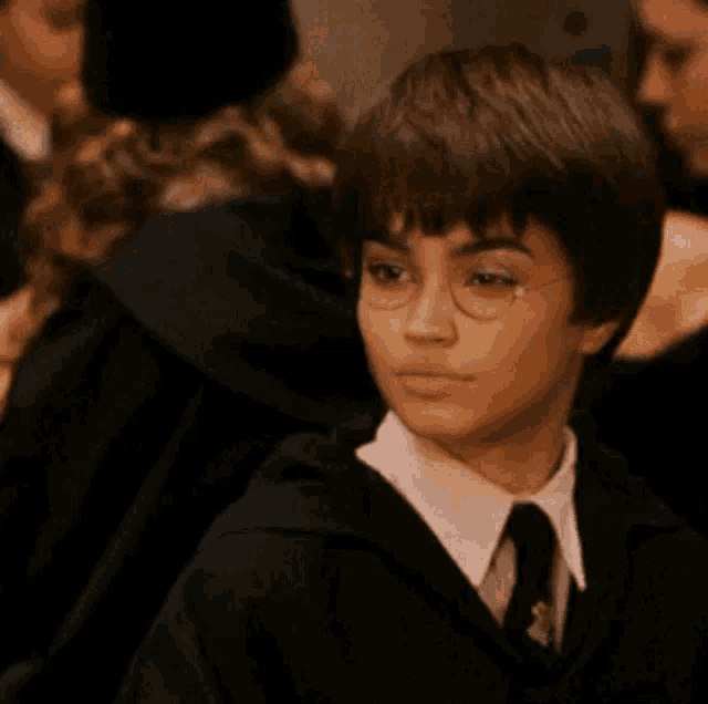 a young boy wearing glasses and a black robe is sitting in a crowd .