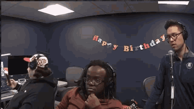 a man wearing headphones stands in front of a banner that says " happy birthday "