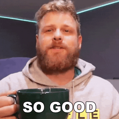 a man with a beard is holding a green coffee mug and says so good