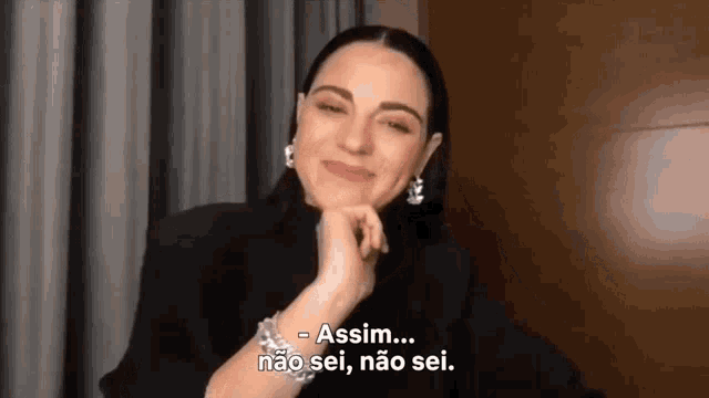 a woman is smiling and talking in a foreign language while wearing a black jacket and earrings .