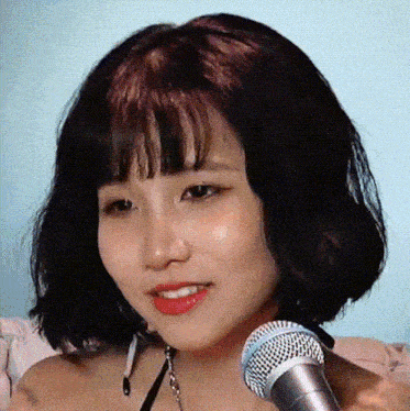 a woman with short black hair and bangs is holding a microphone