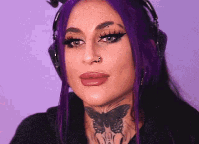 a woman with purple hair is wearing headphones and has a tattoo of a butterfly on her neck .