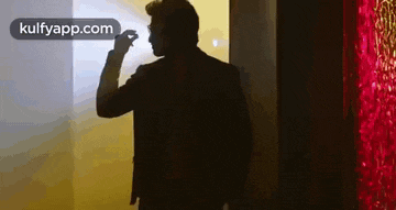 a man in a suit is standing in front of a red wall holding a flashlight .
