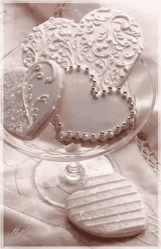 three white heart shaped cookies are sitting on a glass plate on a table .