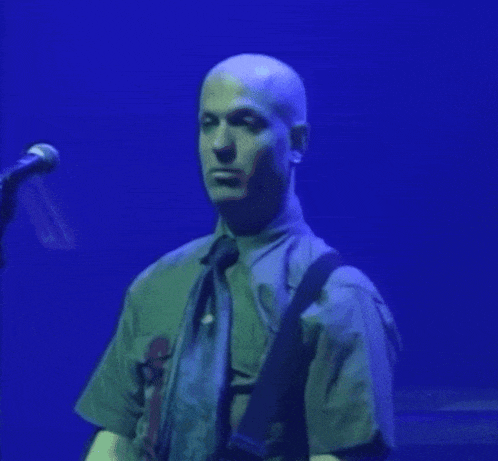 a man in a tie is singing into a microphone while playing a guitar .
