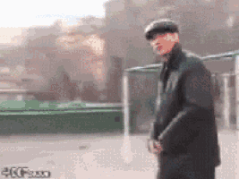 a man wearing a hat and a black jacket is standing in front of a green fence .