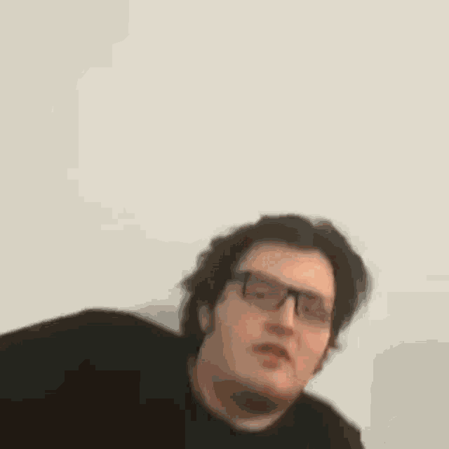 a man wearing glasses and a black shirt is making a face .
