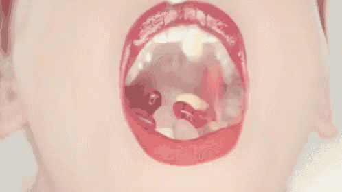 a close up of a woman 's mouth with red lipstick and gummy bears coming out of it .
