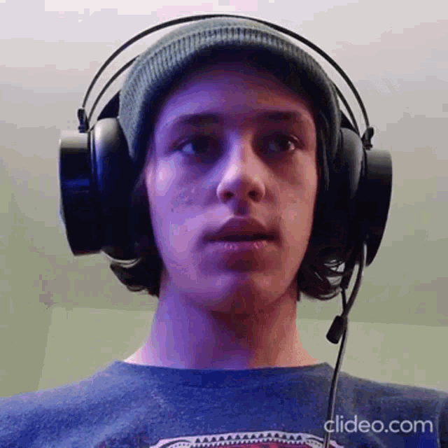 a young man wearing headphones and a hat is looking at the camera .