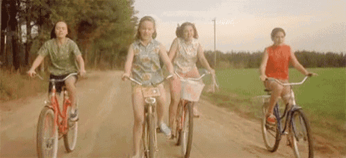 four girls are riding bicycles down a dirt road .