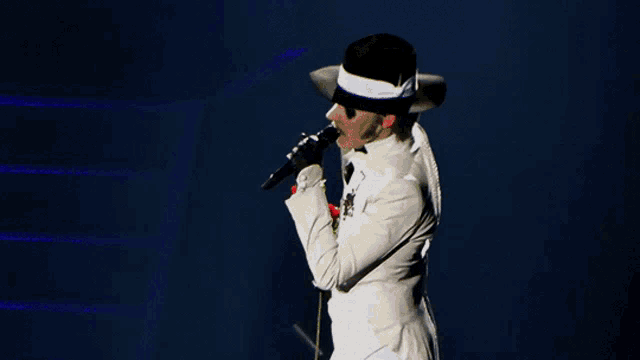 a man in a white suit and fedora is holding a red rose and singing into a microphone