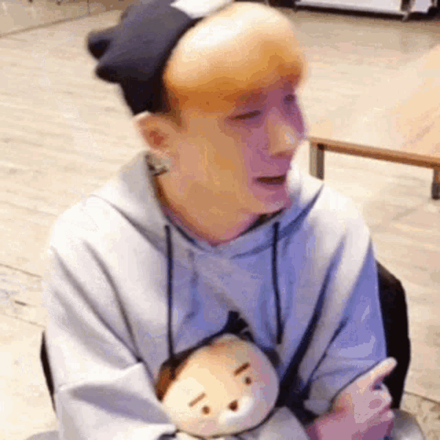 a man wearing a hat and a hoodie is holding a stuffed animal in his lap .