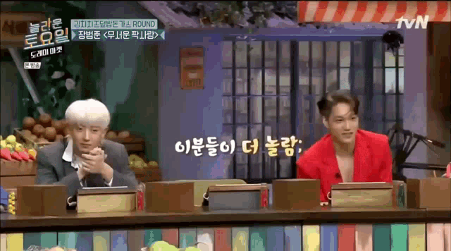 two men sitting at a table in front of a tv screen