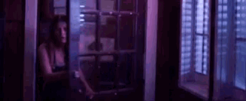 a woman is standing in front of a window in a dark room with purple lights .