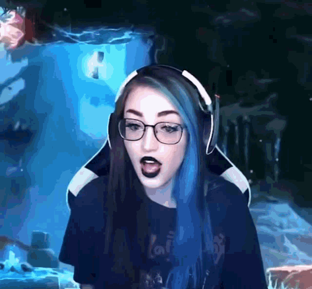 a woman with blue hair and glasses is wearing headphones while playing a video game .