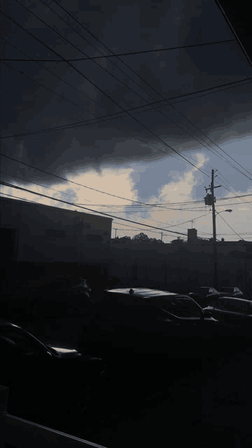 a dark cloudy sky over a parking lot with cars parked in front of a building